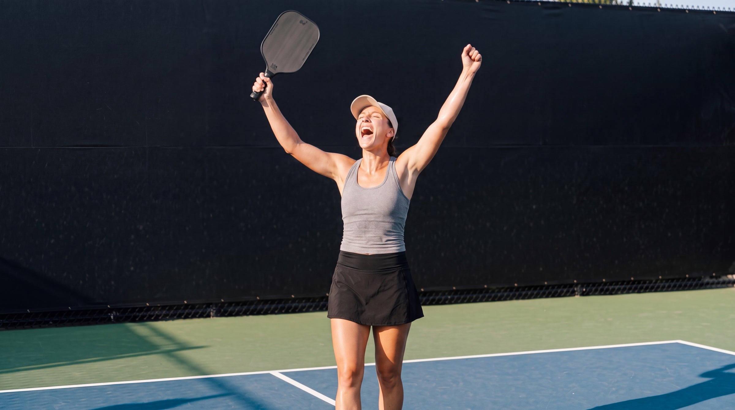 Pickleball player celebrating a winning point with both arms raised, holding a PickleballDoor carbon fibre paddle